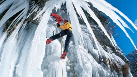 HD desktop wallpaper of an ice climber in red and yellow gear scaling a frozen waterfall against a bright blue sky, capturing the thrill of the sport.