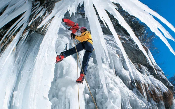HD desktop wallpaper of an ice climber in red and yellow gear scaling a frozen waterfall against a bright blue sky, capturing the thrill of the sport.