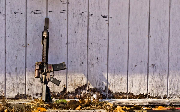 4K Ultra HD PC desktop wallpaper and background: man-made assault rifle propped against a weathered white wooden fence, fallen leaves and a long shadow.