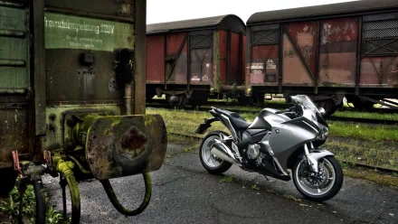A sleek Honda VFR1200F motorcycle parked near weathered train cars, featured as an HD PC desktop wallpaper showcasing the bike and industrial background.