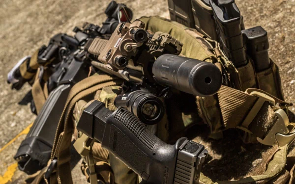 4K Ultra HD PC desktop wallpaper: close-up of man-made firearms — assault rifle, pistol and tactical gear with spare magazines on rough ground.