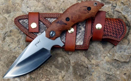 A high-definition desktop wallpaper featuring a beautifully crafted knife with a wooden handle and leather sheath, resting on a textured stone surface.
