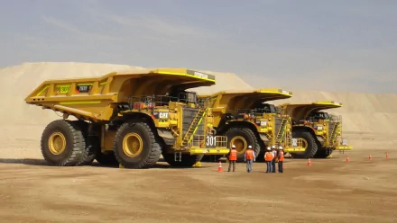 HD wallpaper of large yellow mining trucks parked in a desert environment, with six workers standing nearby.