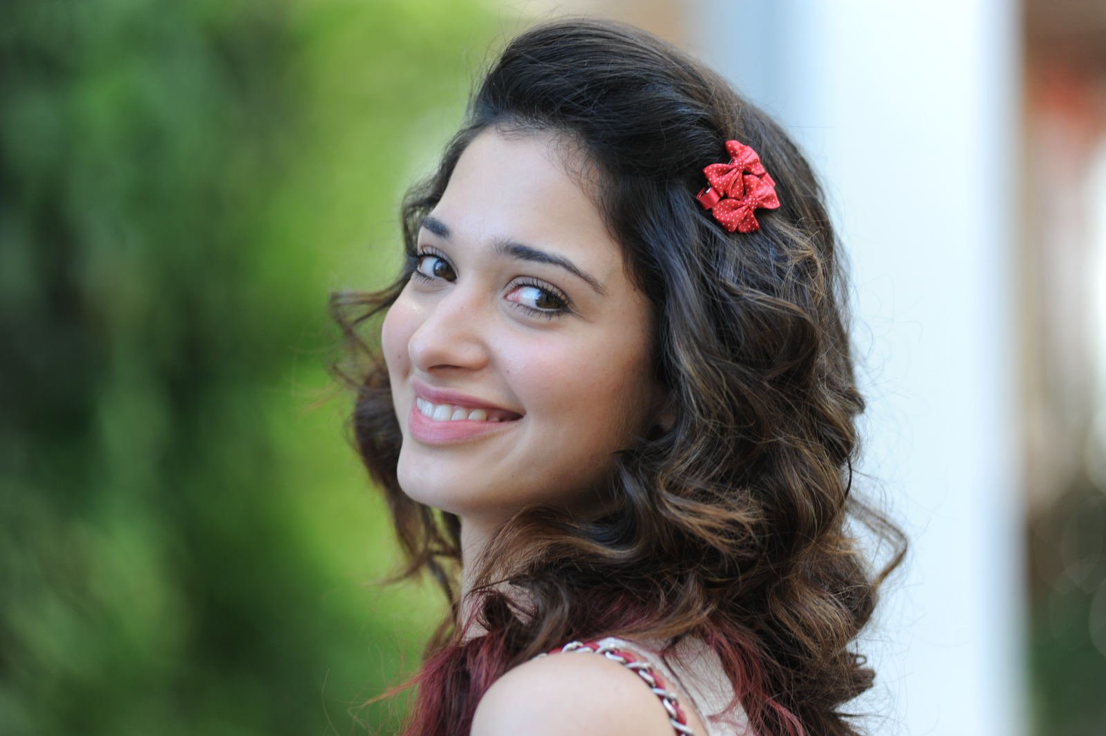A vibrant HD wallpaper featuring the celebrity Tamannaah Bhatia, smiling and looking over her shoulder, complemented by a floral hair accessory and a blurred green background.