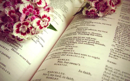 Open book of Shakespeare's Hamlet with delicate pink flowers resting on the pages, captured in a still life photography style for an HD PC desktop wallpaper background.