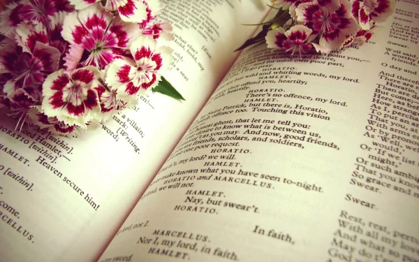 Open book of Shakespeare's Hamlet with delicate pink flowers resting on the pages, captured in a still life photography style for an HD PC desktop wallpaper background.