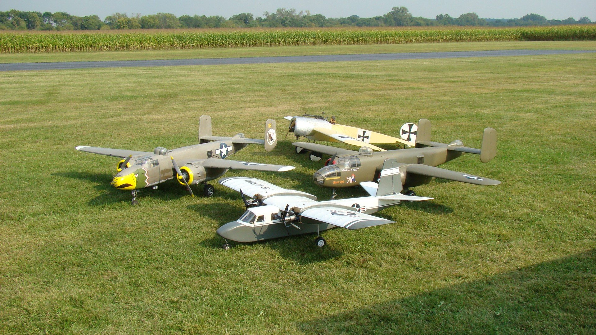 HD PC desktop wallpaper and background of three man-made toy model WWII aircraft parked on a grassy airfield.