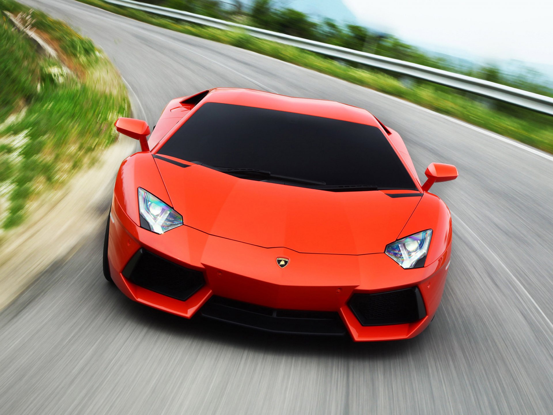 HD PC desktop wallpaper of a vibrant orange Lamborghini Aventador LP 700-4 speeding on a winding road with blurred background.