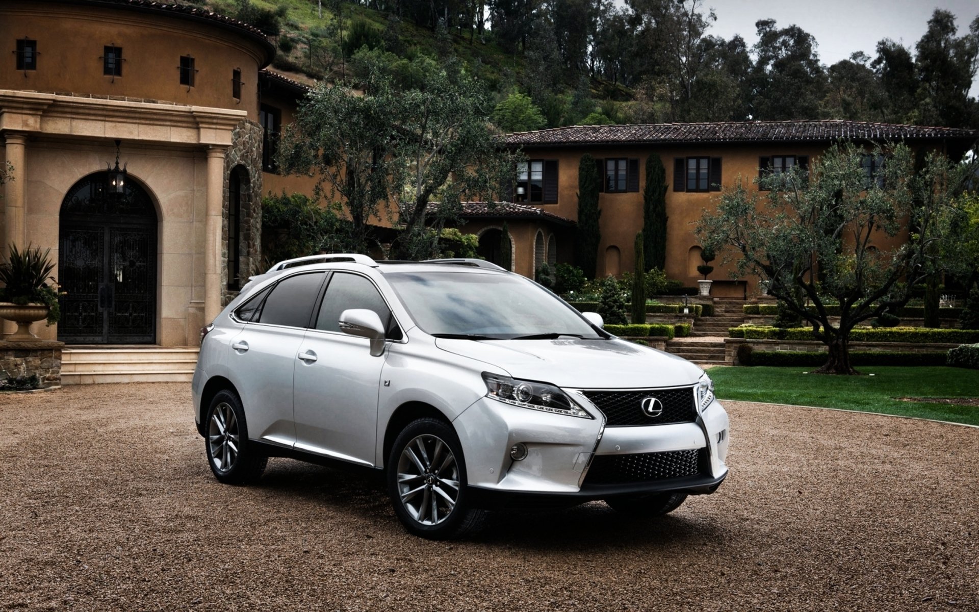 HD PC desktop wallpaper of a silver Lexus vehicle (SUV) parked on a gravel driveway before a Mediterranean-style villa, framed by trees and manicured gardens.