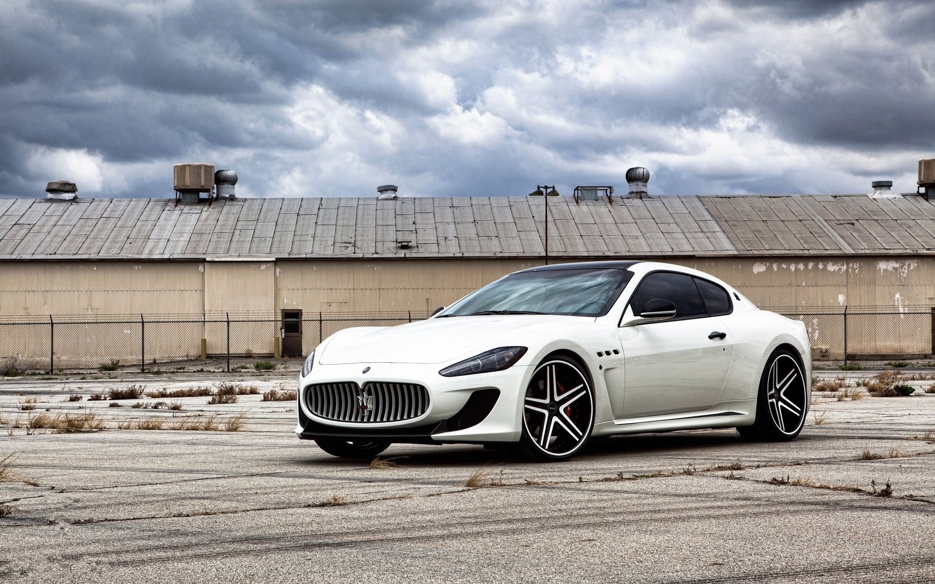 White Maserati sports vehicle on cracked tarmac beneath a dramatic cloudy sky — HD PC desktop wallpaper background