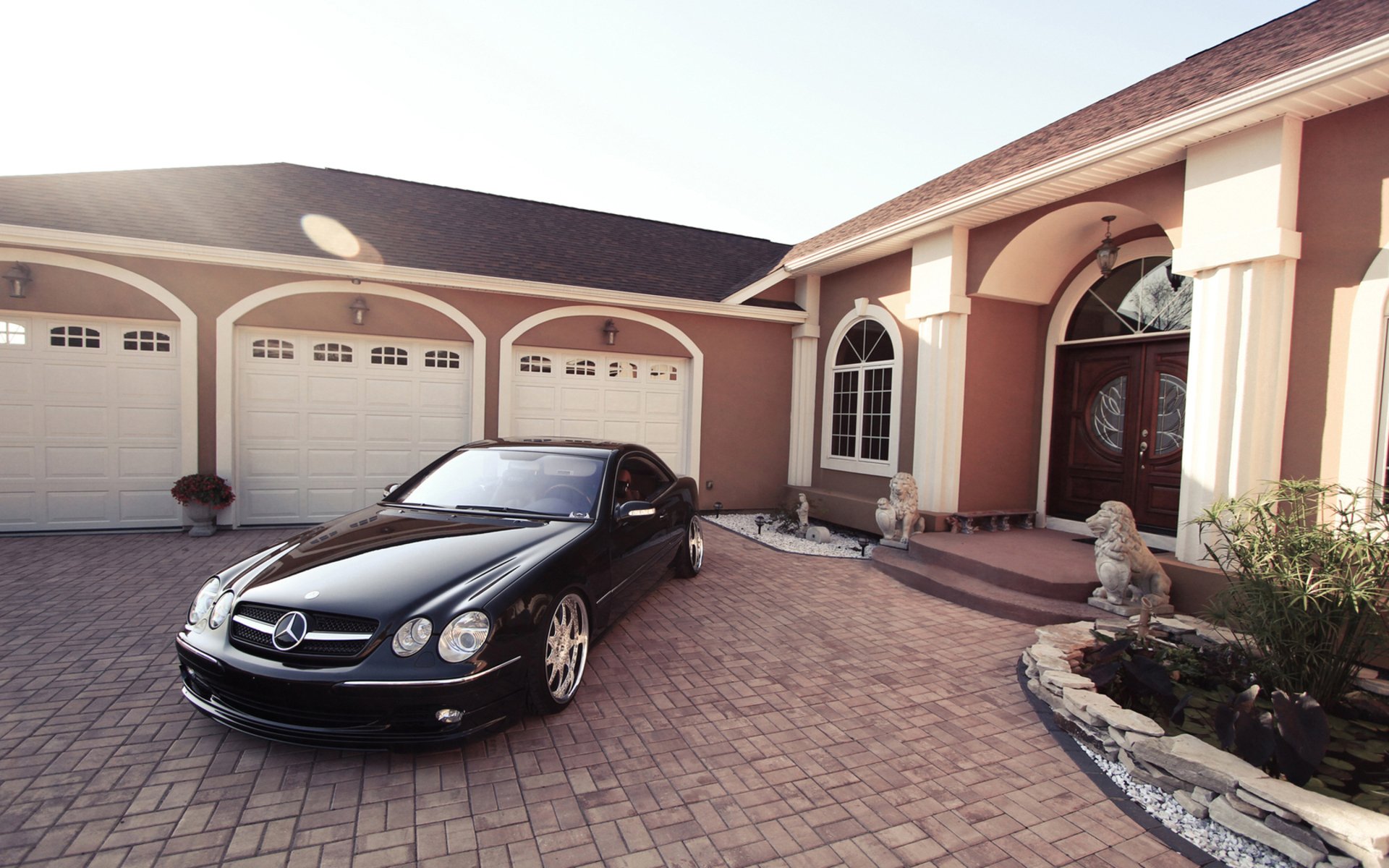 HD PC desktop wallpaper/background: black Mercedes sedan parked on a brick driveway in front of a large stucco house with triple garage and arched entry.