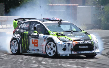 Drifting Ford Focus rally vehicle in Monster livery kicking up smoke on asphalt; dynamic 2K Quad HD PC desktop wallpaper/background.