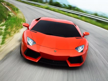 HD PC desktop wallpaper of a vibrant orange Lamborghini Aventador LP 700-4 speeding on a winding road with blurred background.