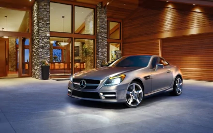 A sleek Mercedes vehicle is parked in front of a modern, stylish house, featuring warm wooden accents and large windows, creating a luxurious atmosphere. HD wallpaper and background.