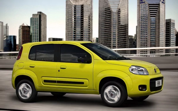 HD PC Desktop Wallpaper and Background: bright yellow Fiat compact vehicle cruising on a city highway with modern glass skyscrapers in the background.