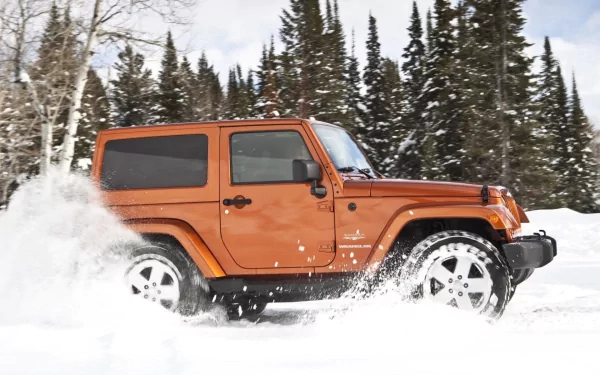 An orange Jeep driving through a snowy landscape, surrounded by tall evergreen trees, creating a dynamic and adventurous scene for a HD desktop wallpaper.