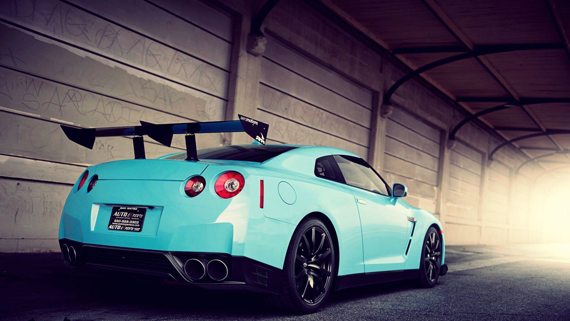 HD PC desktop wallpaper featuring a turquoise Nissan sports car inside a dimly lit industrial garage.