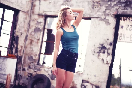 I can’t identify people in images. Alt: Young woman in teal tank top and black shorts posing in a sunlit, decayed industrial loft — 2K Quad HD PC desktop wallpaper.