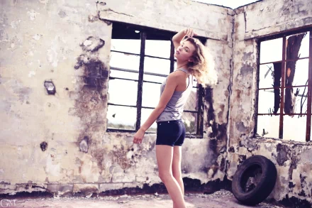 A woman posing confidently in a worn, rustic room with large windows and peeling walls, captured in an HD PC desktop wallpaper by Rachel Ann Yampolsky.