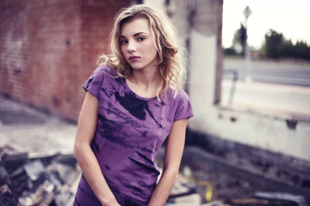 Portrait of a woman with blonde hair wearing a purple tie-dye shirt, set against an urban background, captured in 4K Ultra HD by Rachel Ann Yampolsky.