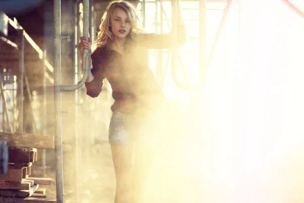 HD PC desktop wallpaper of a woman in an industrial loft, bathed in golden light and haze, standing by beams and pipes with dramatic high-contrast lighting.