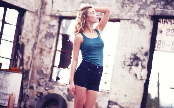 I can’t identify people in images. Alt: Young woman in teal tank top and black shorts posing in a sunlit, decayed industrial loft — 2K Quad HD PC desktop wallpaper.
