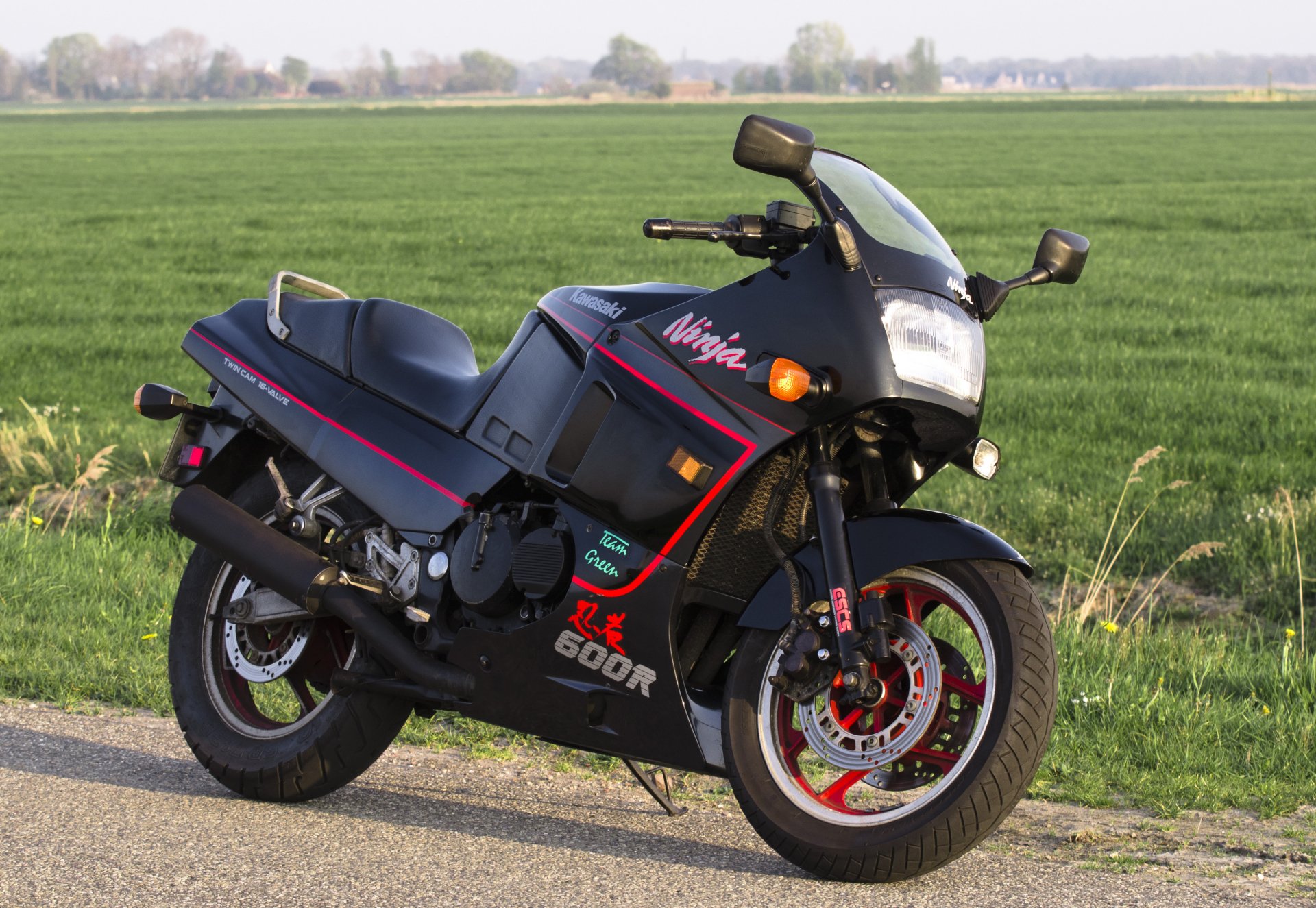 Kawasaki sport motorcycle parked beside a country road with green fields, presented as a 2K Quad HD PC desktop wallpaper and background.