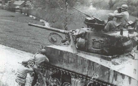 Black-and-white HD PC desktop wallpaper of a military M4 Sherman tank with soldiers aboard and beside it, rolling along a rural road past village houses.