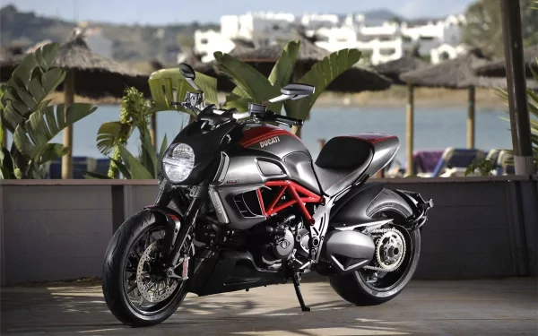 HD PC desktop wallpaper showcasing a sleek Ducati motorcycle parked indoors with a scenic waterfront and white buildings in the blurred background.