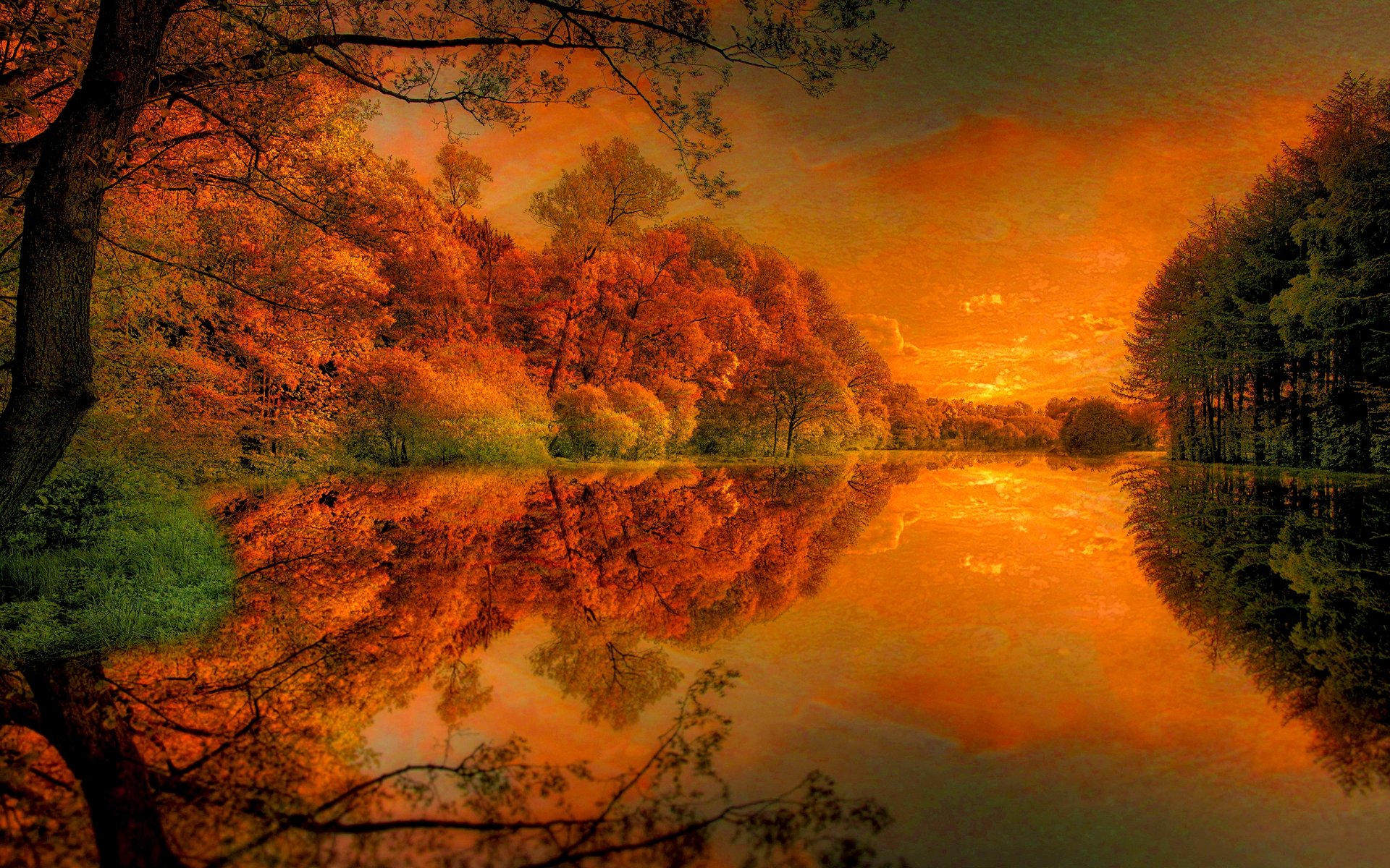 HD desktop wallpaper featuring a serene lake surrounded by autumnal trees with vibrant orange leaves, reflecting on the calm water under a fiery sunset sky. Background setting in nature.