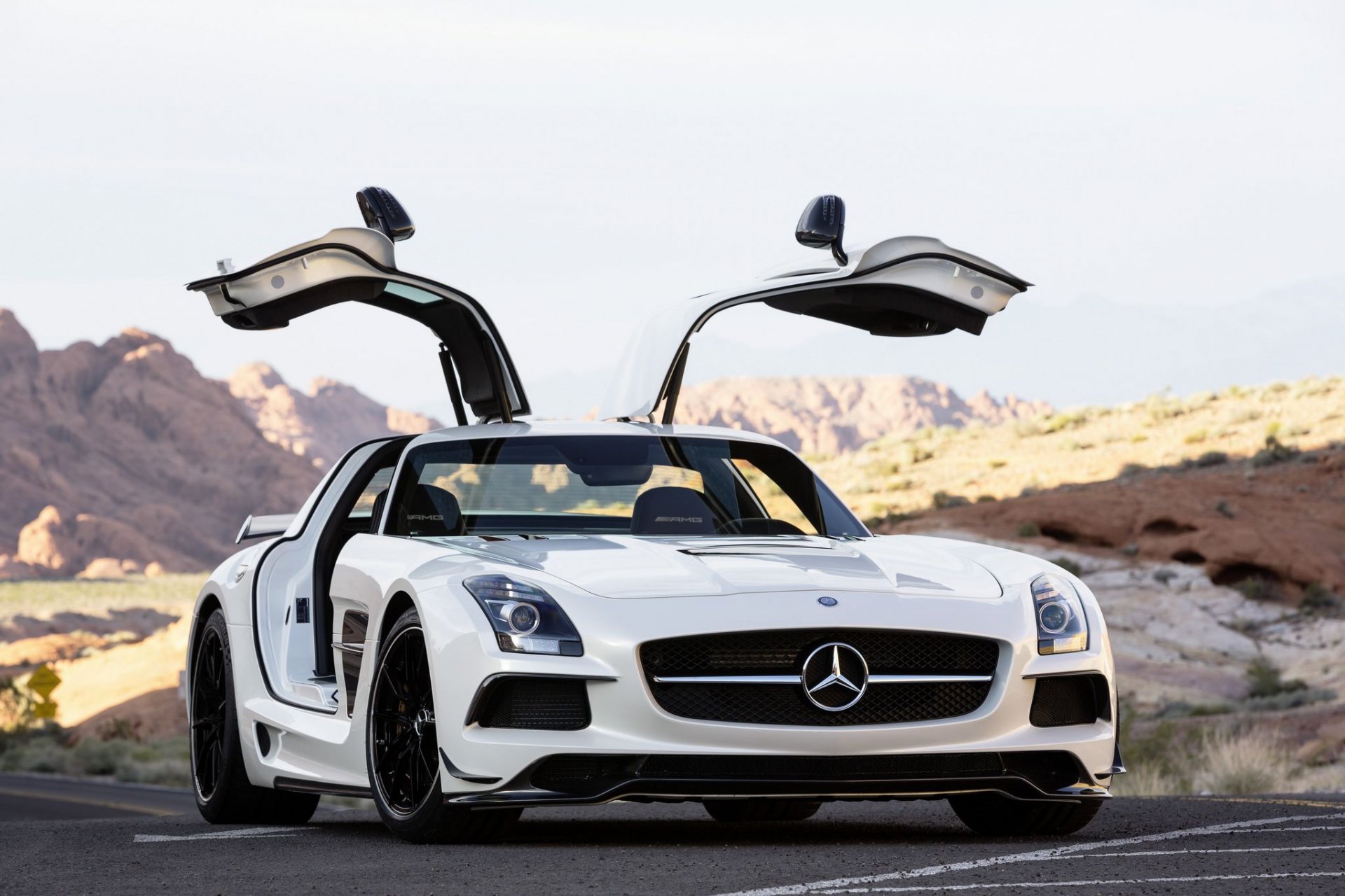 White Mercedes-Benz SLS AMG with gullwing doors open, set against a desert landscape; HD PC desktop wallpaper showcasing this luxury vehicle.
