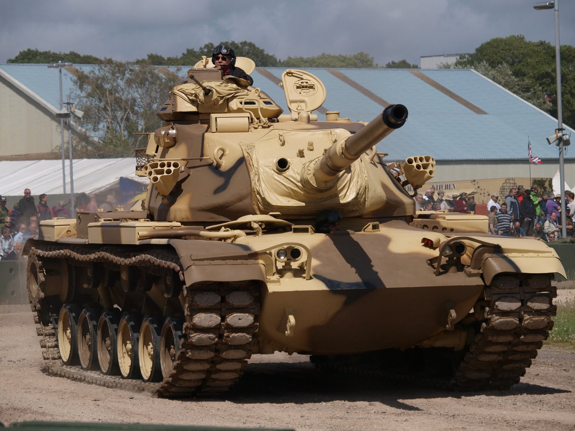 HD PC desktop wallpaper featuring a military tank in desert camouflage, with crew members visible and spectators in the background.