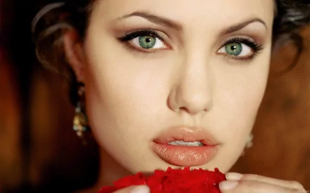 HD desktop wallpaper featuring Angelina Jolie with green eyes and glossy lips, holding a red object close to her face against a warm background.