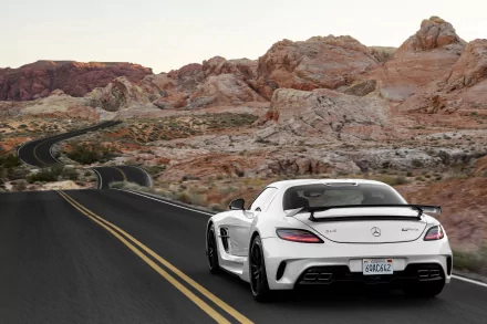 A sleek white Mercedes-Benz SLS AMG parked on a winding road, surrounded by stunning red rock formations, showcasing its powerful design against a breathtaking landscape.