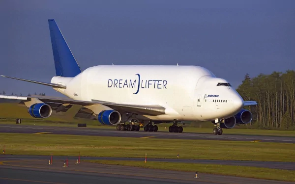 5K Ultra HD PC desktop wallpaper and background: Boeing Dreamlifter cargo aircraft taxiing on runway at dusk, white fuselage, blue tail and tree-lined horizon.