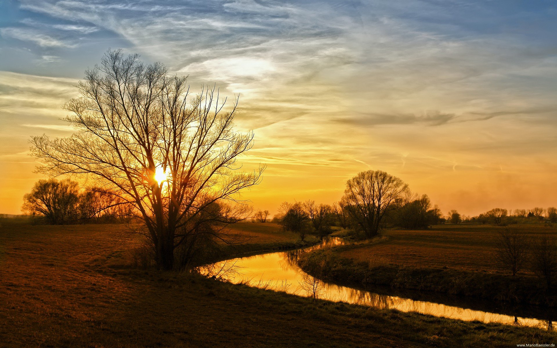 HD desktop wallpaper showing a serene river winding through a landscape with trees at sunset under a partly cloudy sky.