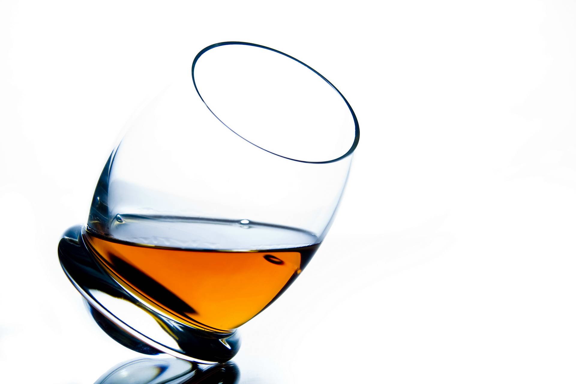 A close-up of a tilted glass containing amber liquor against a clean white background, creating a sleek and modern desktop wallpaper.
