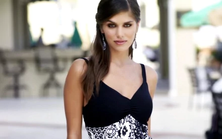 A confident woman in a stylish black and white dress poses for the camera, set against a blurred outdoor background. This HD wallpaper features Anahi Gonzales.