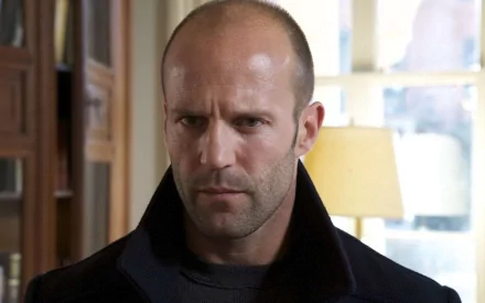 HD wallpaper featuring Jason Statham, capturing a serious expression as he looks off-camera, set against an interior background with soft lighting.
