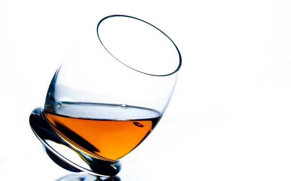 A close-up of a tilted glass containing amber liquor against a clean white background, creating a sleek and modern desktop wallpaper.