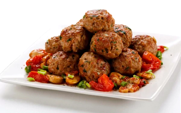 A delicious arrangement of golden-brown meatballs garnished with fresh herbs and served with sautéed tomatoes and garlic, showcasing the flavors of Greek and Italian cuisine.