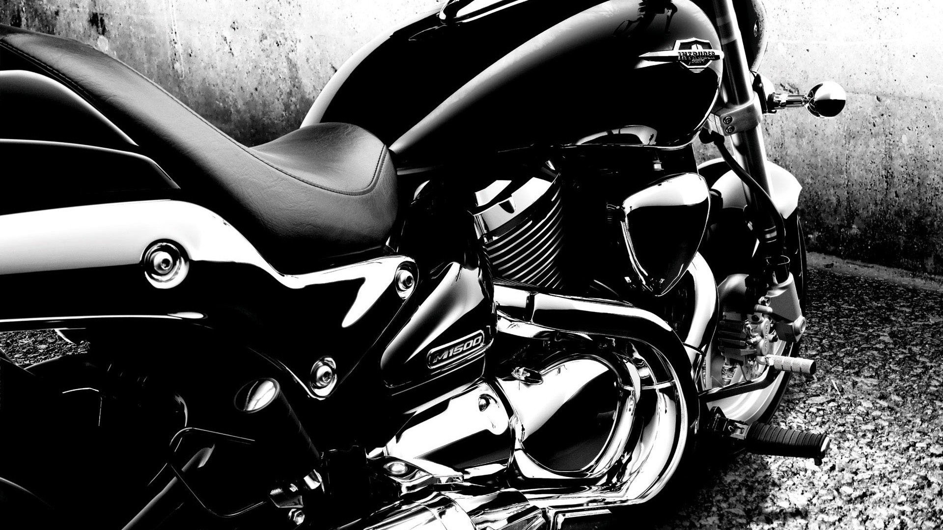 Black-and-white HD PC desktop wallpaper of a Suzuki vehicle—cruiser motorcycle close-up of seat, fuel tank and chrome engine against a textured wall.