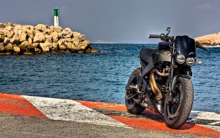 Buell vehicle: black sport motorcycle parked on a harbor edge beside rocky jetty and lighthouse — vivid HD PC desktop wallpaper and background.