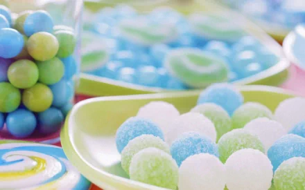 HD PC desktop wallpaper featuring colorful, round sugar-coated candies in pastel blue, green, and white hues on a yellow plate with additional candy jars in the background.
