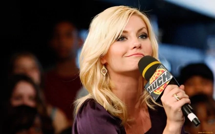 Elisha Cuthbert smiles while holding a microphone, captured in a lively moment on stage. This image serves as a vibrant HD desktop wallpaper and background.