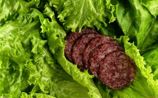 HD desktop wallpaper featuring close-up of sliced salami nestled on fresh green lettuce leaves, highlighting food textures and vibrant colors.