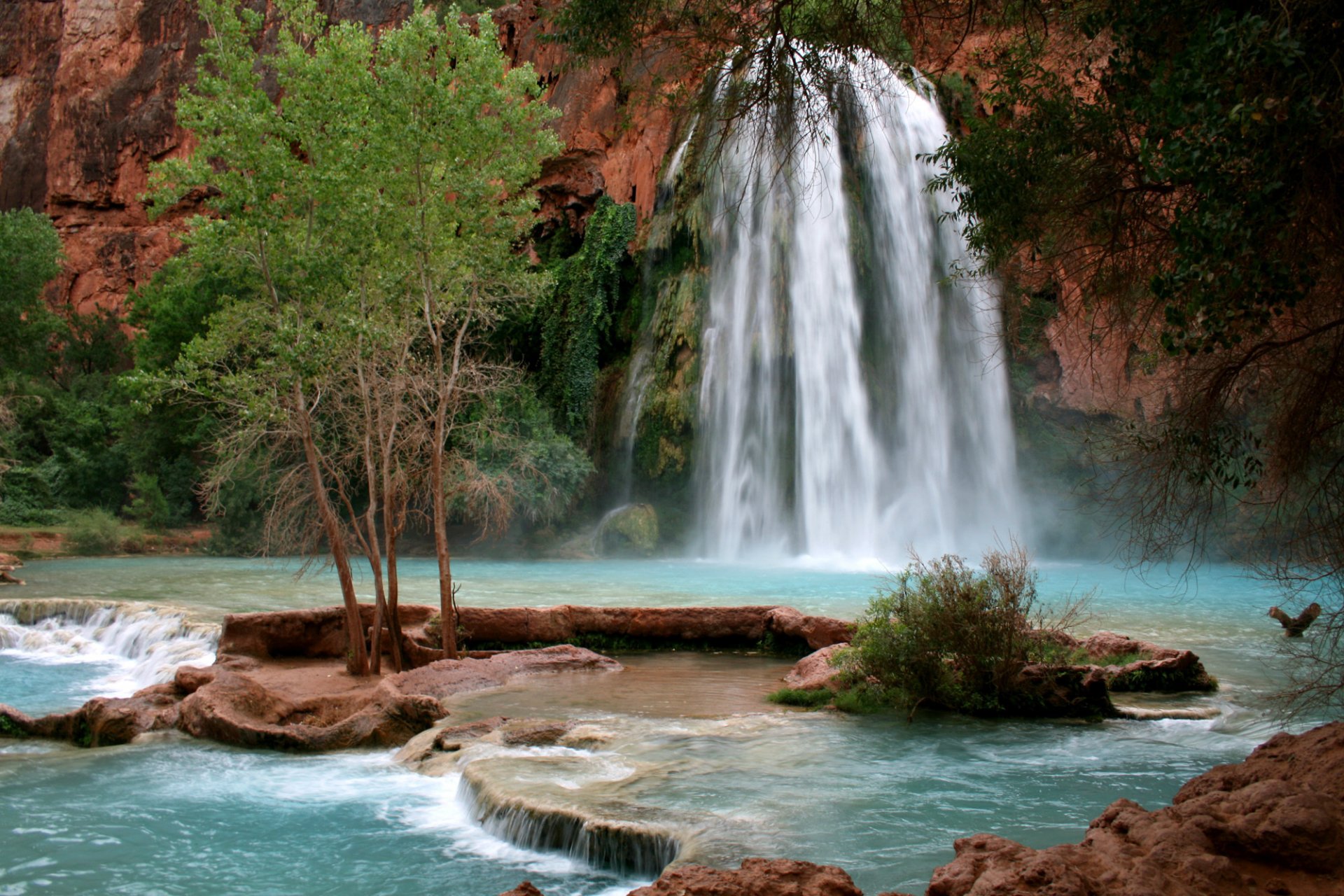 A stunning waterfall cascades into a turquoise pool, surrounded by lush greenery and rocky formations, showcasing the beauty of nature in this HD desktop wallpaper.