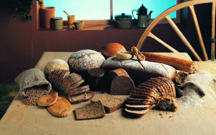 HD PC desktop wallpaper featuring an assortment of freshly baked bread loaves and slices arranged on a rustic table, highlighted by warm, natural lighting.