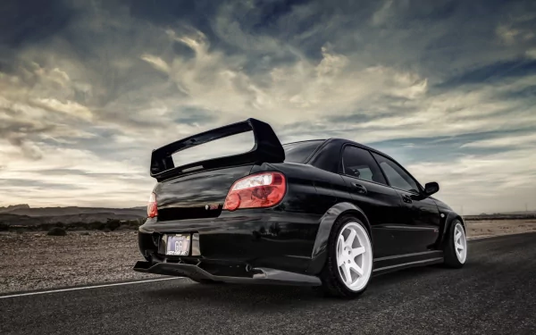 A sleek black Subaru parked on a deserted road under a dramatic sky, featuring a prominent rear spoiler and striking white wheels, presented as a 4K Ultra HD desktop wallpaper.