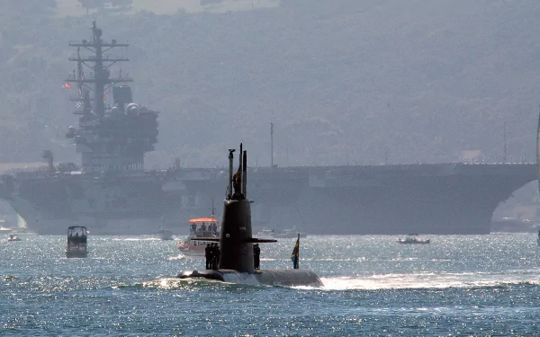 Military submarine surfacing in coastal waters with an aircraft carrier looming in the distance — 4K Ultra HD PC desktop wallpaper and background.